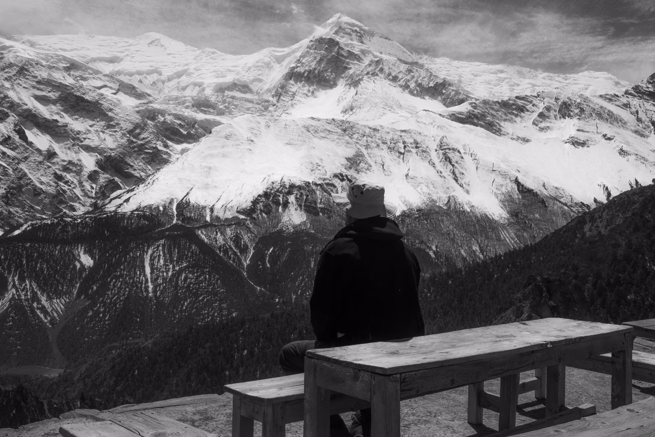 A man sitting on a bench watching a Himalayan mountain range