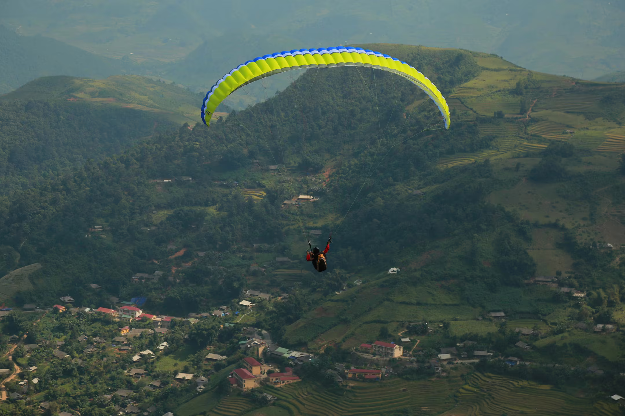 A solo paraglider over terraced green hills